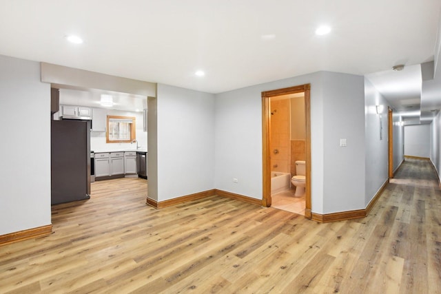 unfurnished living room featuring light wood finished floors, baseboards, a sink, and recessed lighting