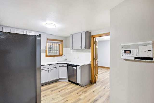 kitchen with tasteful backsplash, stainless steel appliances, gray cabinetry, light wood-type flooring, and a sink