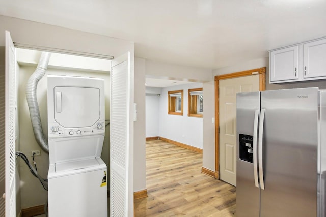 washroom featuring light wood-type flooring, laundry area, baseboards, and stacked washer and clothes dryer