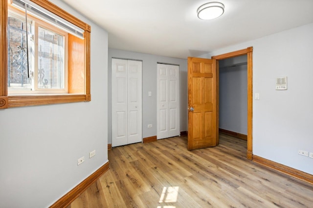 unfurnished bedroom with light wood finished floors, baseboards, and multiple closets