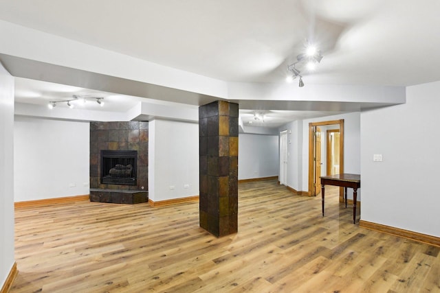 finished below grade area with light wood finished floors, track lighting, a tiled fireplace, and baseboards