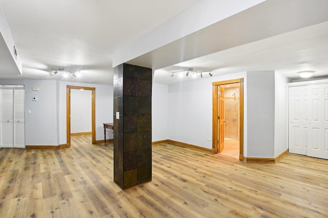 finished basement featuring track lighting, light wood-style flooring, and baseboards