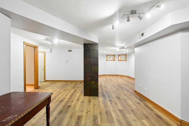 finished basement with rail lighting, visible vents, light wood-style flooring, and baseboards