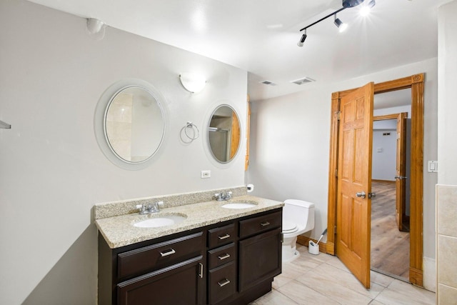 bathroom featuring toilet, double vanity, visible vents, and a sink