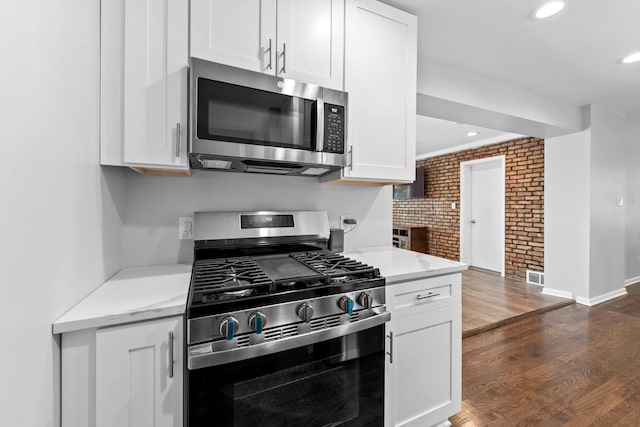 kitchen featuring brick wall, visible vents, white cabinetry, appliances with stainless steel finishes, and dark wood finished floors