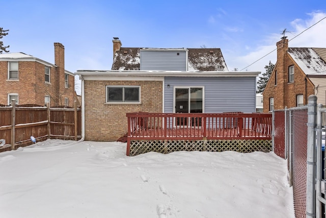 snow covered property with brick siding, fence, a chimney, and a wooden deck