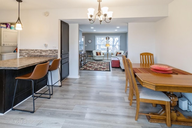 dining room featuring recessed lighting, stacked washer and dryer, light wood-style flooring, and an inviting chandelier