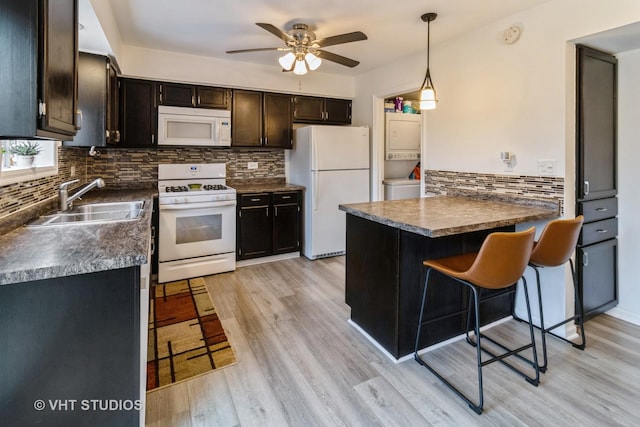 kitchen with white appliances, dark countertops, light wood-style flooring, a peninsula, and a sink