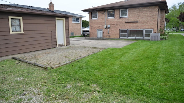 back of property featuring brick siding, a yard, a chimney, central AC unit, and a patio area