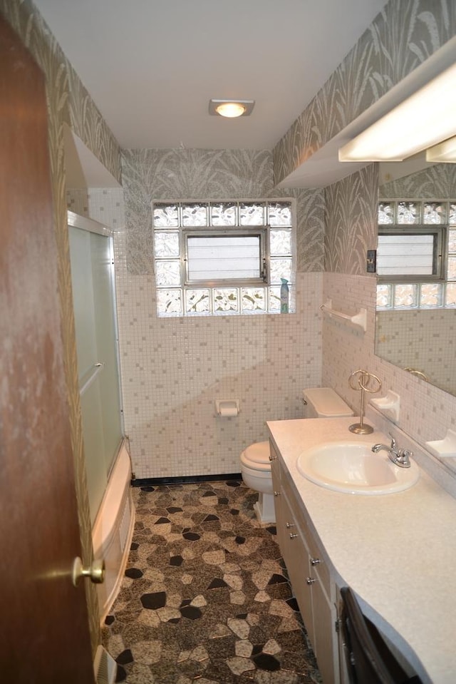 full bath featuring wallpapered walls, toilet, enclosed tub / shower combo, vanity, and tile walls