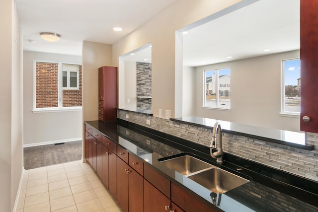 kitchen with light tile patterned floors, tasteful backsplash, baseboards, dark stone counters, and a sink