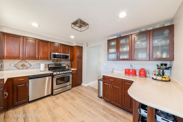 kitchen with decorative backsplash, light countertops, glass insert cabinets, light wood-style floors, and appliances with stainless steel finishes