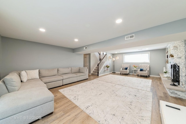 living room featuring stairway, visible vents, recessed lighting, a stone fireplace, and light wood-style floors