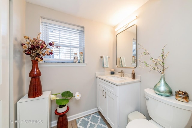 half bath featuring vanity, toilet, and baseboards