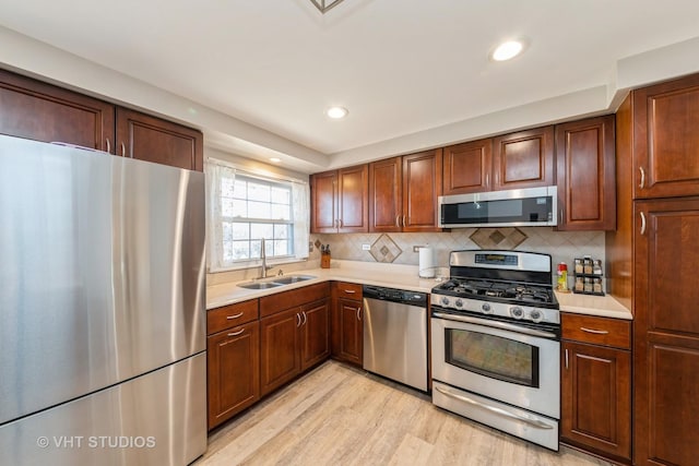 kitchen featuring light wood finished floors, stainless steel appliances, light countertops, and a sink