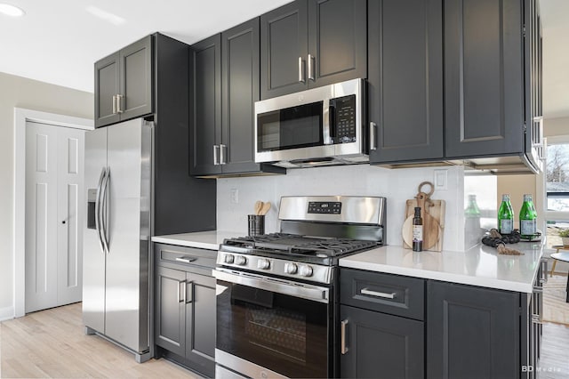 kitchen featuring light wood-type flooring, stainless steel appliances, backsplash, and light countertops