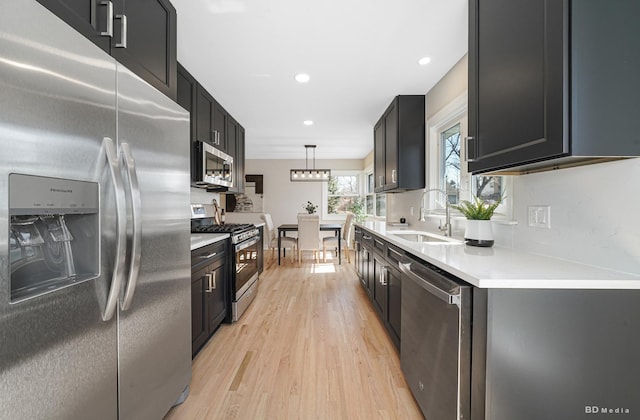 kitchen with a sink, stainless steel appliances, light countertops, decorative light fixtures, and light wood-type flooring