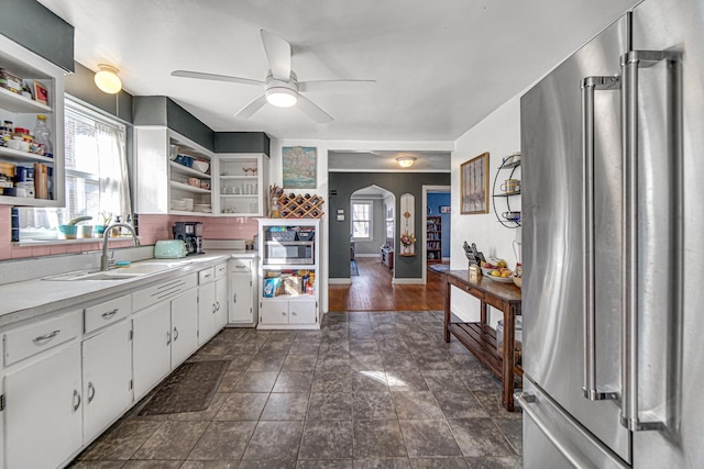 kitchen with arched walkways, open shelves, high end fridge, light countertops, and a sink