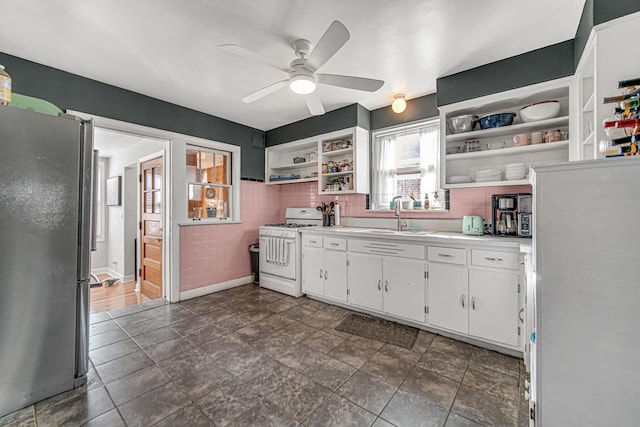 kitchen with white range with gas cooktop, freestanding refrigerator, white cabinetry, open shelves, and a sink