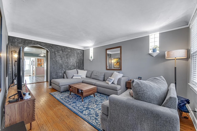 living area with baseboards, crown molding, arched walkways, and wood finished floors