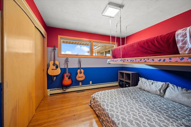 bedroom with a closet, baseboard heating, and wood finished floors