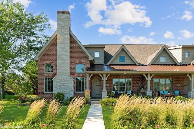 view of front of house featuring metal roof, brick siding, a shingled roof, a standing seam roof, and a chimney