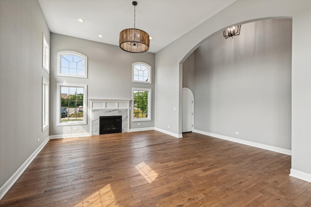 unfurnished living room with arched walkways, a fireplace, baseboards, and wood finished floors