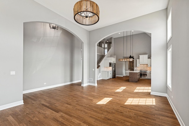 unfurnished living room with plenty of natural light, a notable chandelier, baseboards, and wood finished floors