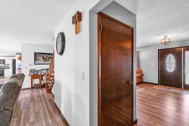 foyer entrance featuring a textured ceiling, stairway, light wood-style flooring, and baseboards