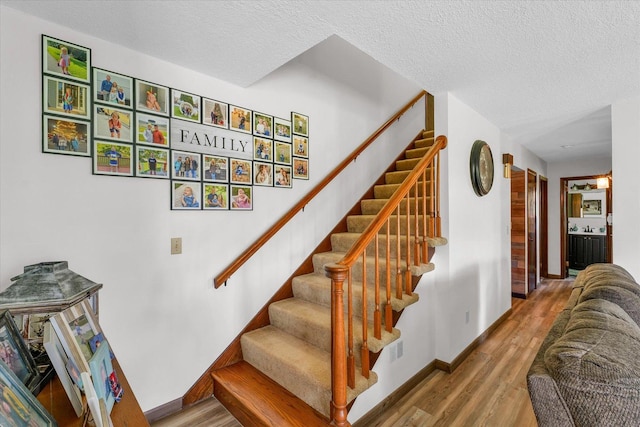 stairs featuring a textured ceiling, wood finished floors, and baseboards