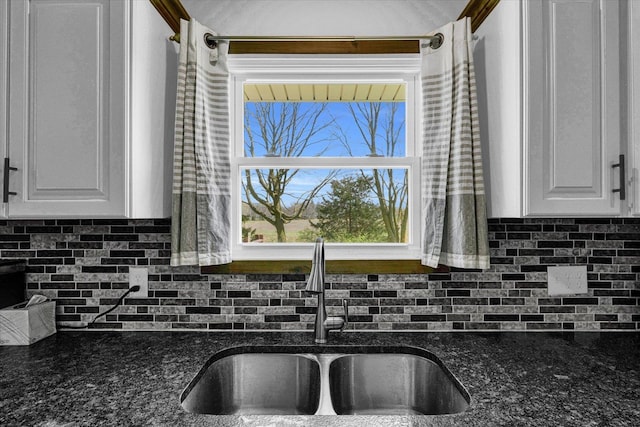 kitchen featuring tasteful backsplash, dark stone countertops, white cabinets, and a sink