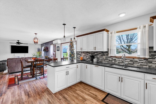 kitchen featuring an AC wall unit, a peninsula, a sink, and light wood-style floors