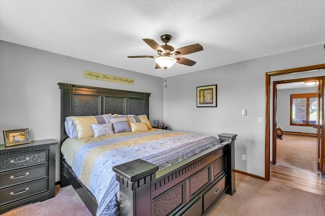 bedroom with a ceiling fan, light carpet, a textured ceiling, and baseboards