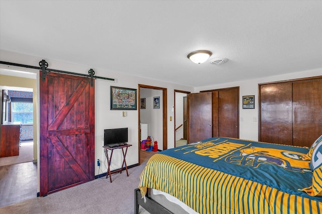 carpeted bedroom with a barn door, visible vents, and multiple closets