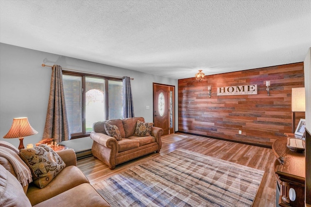 living area with an accent wall, wood finished floors, a textured ceiling, wood walls, and a baseboard heating unit