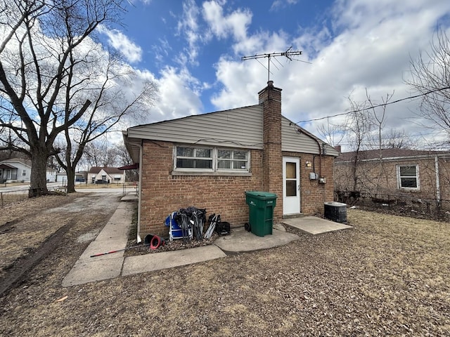 back of property featuring central AC, brick siding, and a chimney