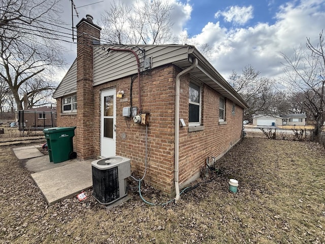 view of side of property with brick siding, fence, a chimney, and central AC unit