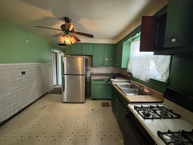 kitchen with range with gas stovetop, freestanding refrigerator, light floors, green cabinets, and a sink