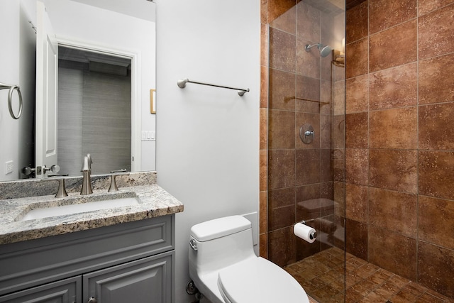 bathroom with toilet, a tile shower, and vanity