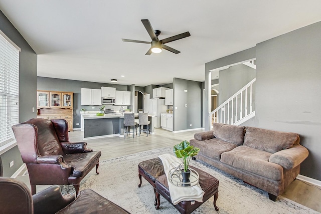 living area with baseboards, stairway, a ceiling fan, and light wood-style floors