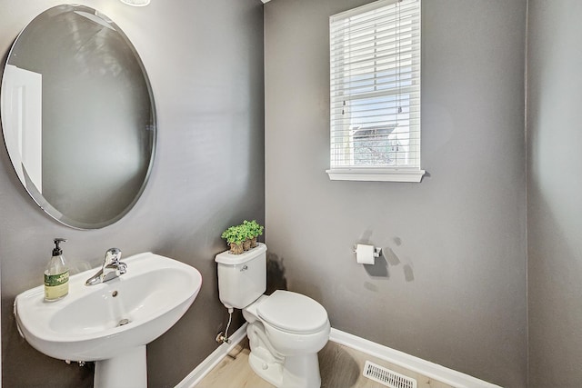 half bathroom featuring baseboards, visible vents, toilet, wood finished floors, and a sink