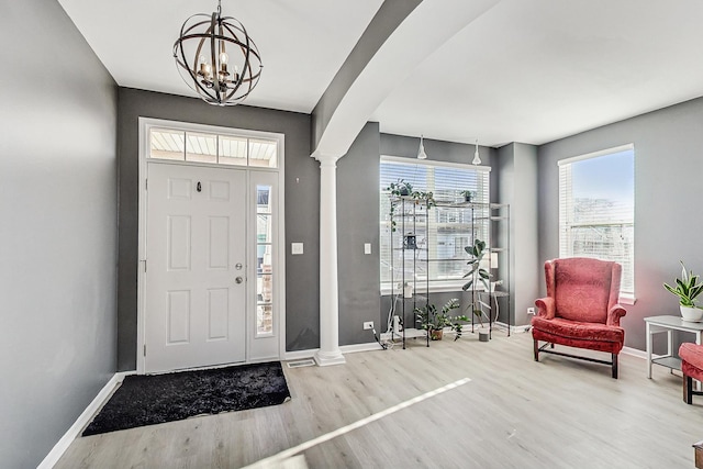 entrance foyer featuring arched walkways, a notable chandelier, decorative columns, wood finished floors, and baseboards