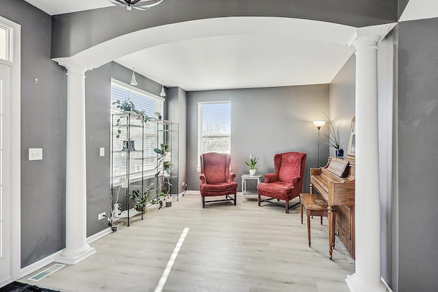 living area featuring arched walkways, wood finished floors, visible vents, baseboards, and ornate columns