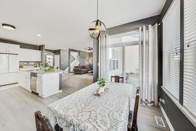 dining area featuring ceiling fan, visible vents, baseboards, light wood-style floors, and stairway