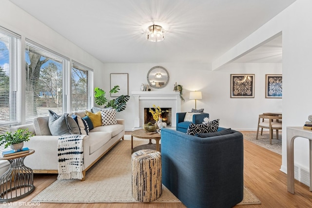 living room featuring beam ceiling, baseboards, a lit fireplace, and light wood finished floors