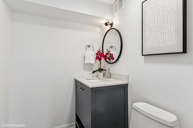 half bath with toilet, vanity, visible vents, and baseboards