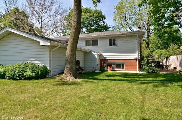 rear view of house featuring brick siding, a lawn, a chimney, and fence