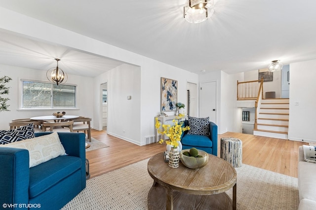 living area with baseboards, stairway, wood finished floors, and an inviting chandelier