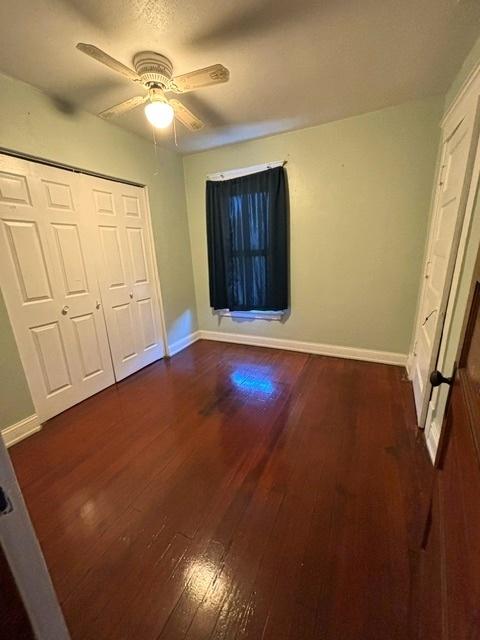 unfurnished bedroom with a closet, dark wood finished floors, baseboards, and ceiling fan