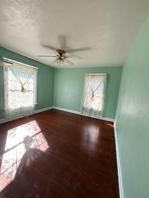 unfurnished room featuring plenty of natural light, a textured ceiling, baseboards, and wood finished floors